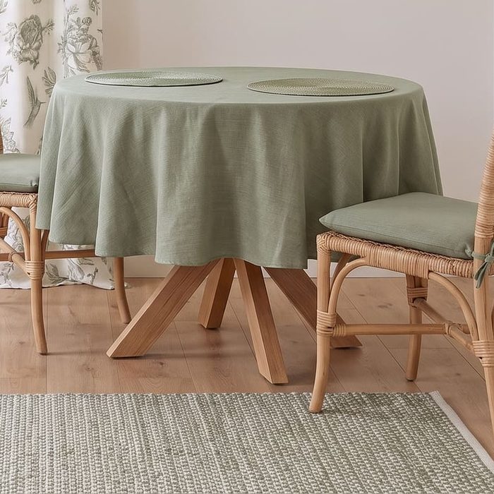 A round table in a sage cloth with woven placemats and a sage chair pad