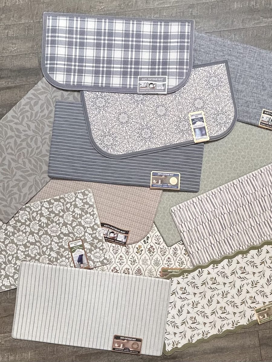 Our anti-fatigue mats fanned out on a wood floor: plaids, florals, leaf prints and textures